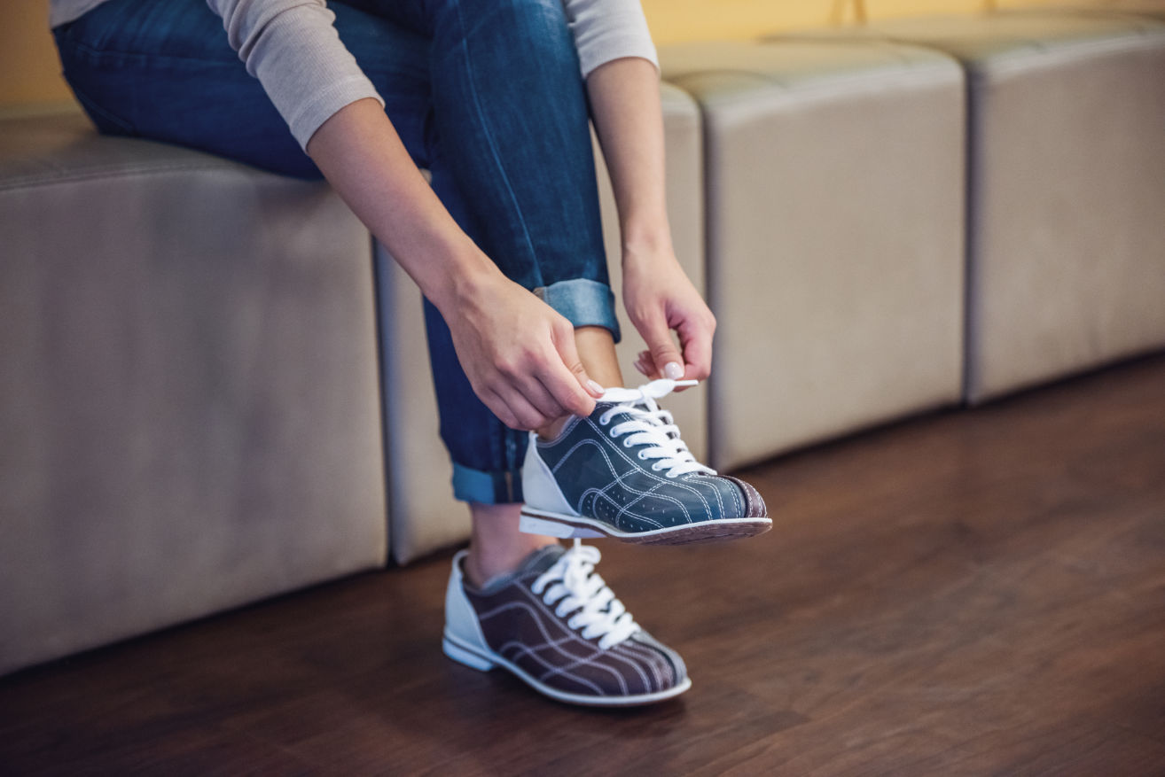 Frau zieht sich Bowling-Leihschuhe an: Die Schuhe vorher zu desinfizieren kann dabei helfen, Nagelpilz vorzubeugen.